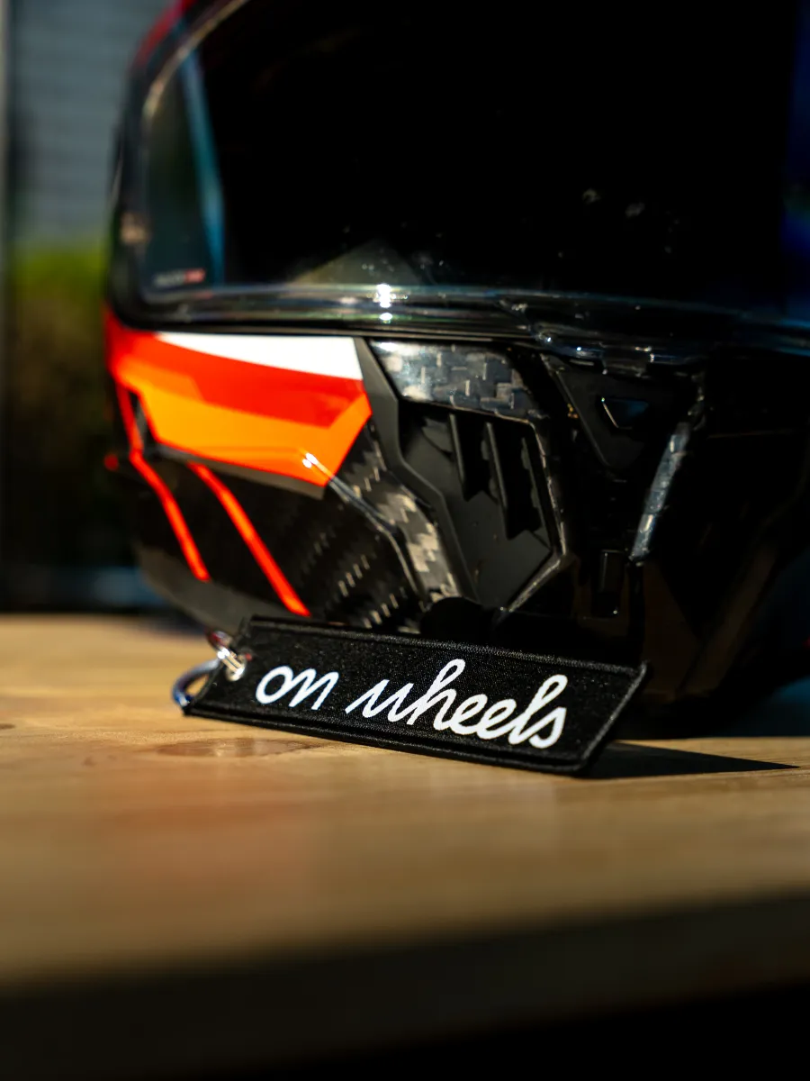 Porte-clés On Wheels posé devant un casque de moto, accessoire motard lifestyle