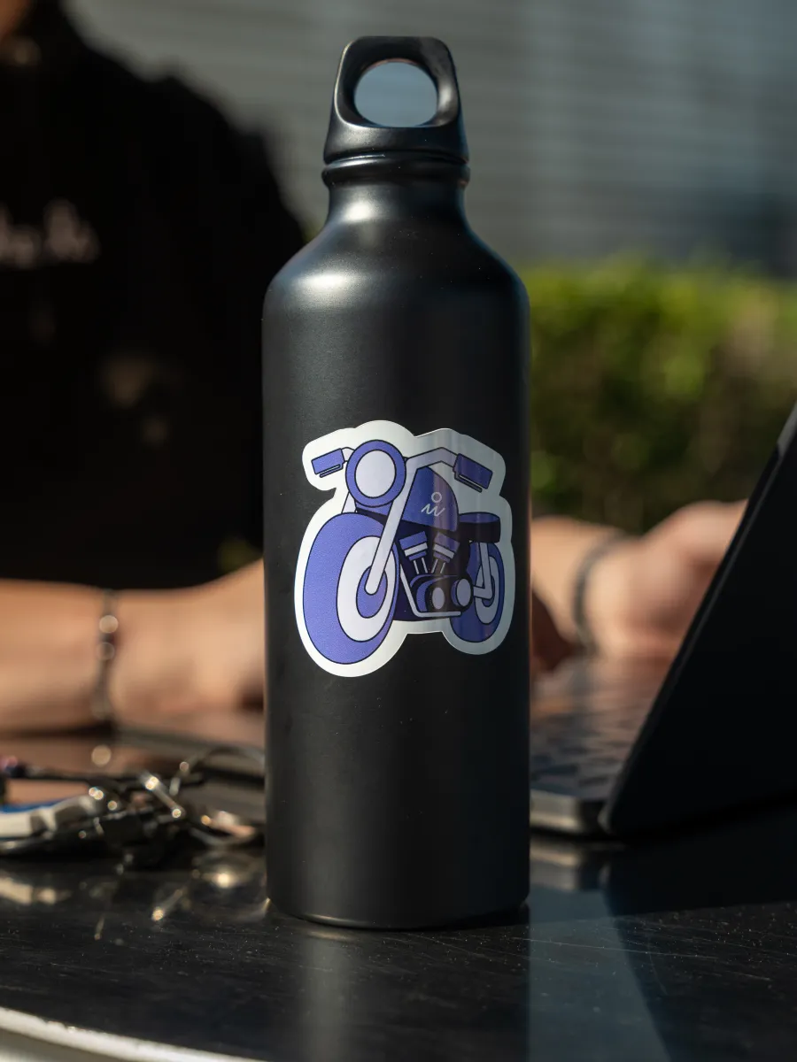 Gourde noire décorée d’un sticker moto On Wheels posée sur une table